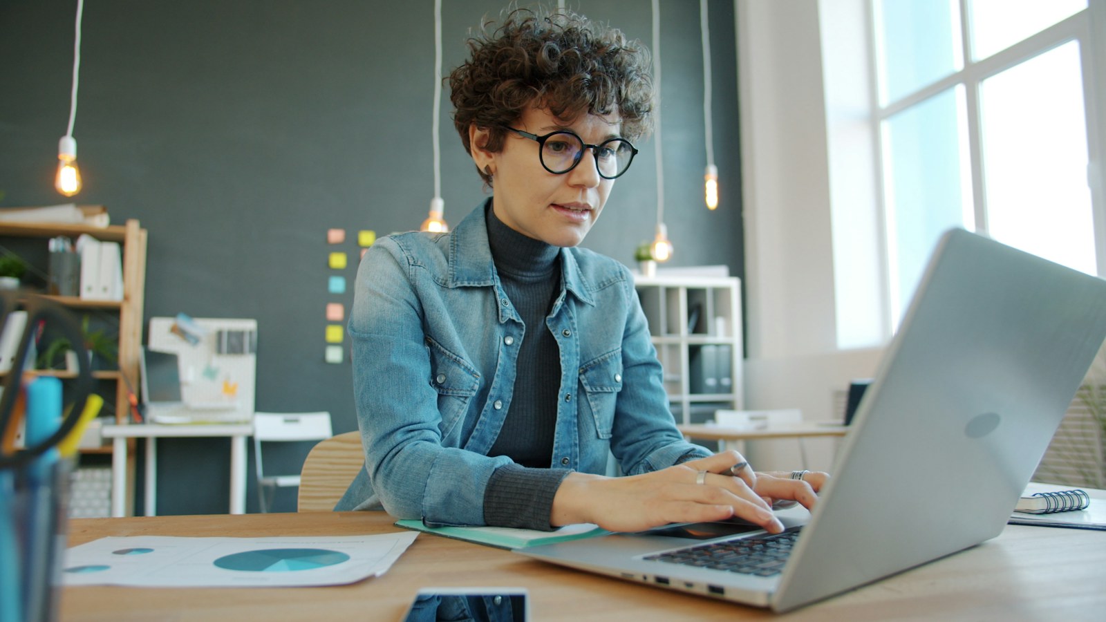 Una profesional trabaja concentrada en una computadora en una oficina luminosa.